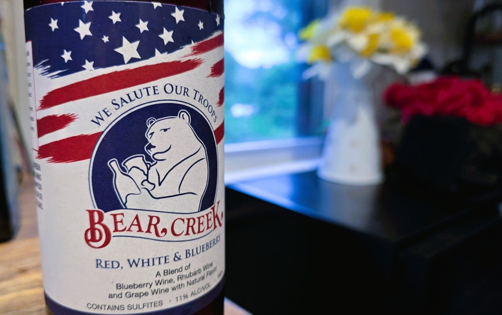 Close up of the wine label that says "We Salute Our Troops, Bear Creek, Red, White ad Blueberry, A blend of Blueberry Wine, Rhubarb wine and grape wine with natural flavors, contains sulfites, 11% alcohol.