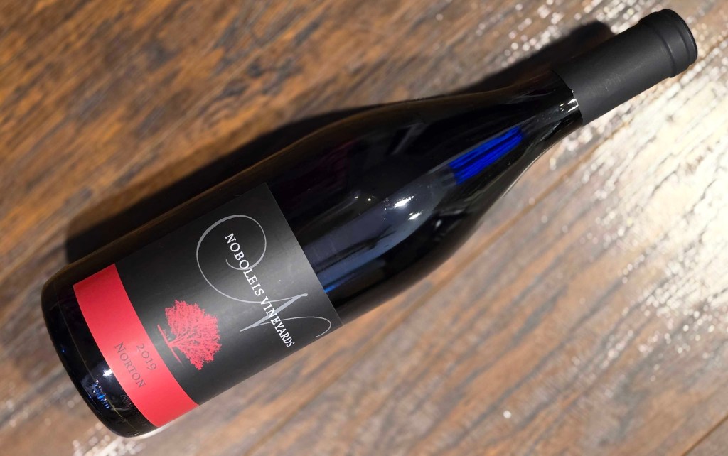 Bottle of wine on a wood floor. The label is black and red.